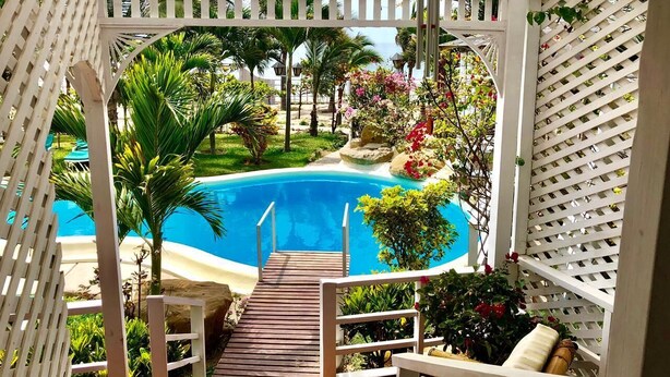 A wooden deck leading to a pool surrounded by lush greenery and a white pergola structure. - Beautiful Oceanfront Home in Zorritos - Just 2 Hours from Tumbes Airport (tumbes)