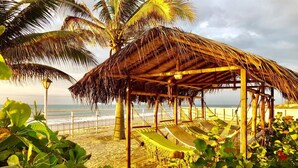 A beach hut with a thatched roof, surrounded by lush greenery and palm trees, overlooking the ocean. - Beautiful Oceanfront Home in Zorritos - Just 2 Hours from Tumbes Airport (tumbes)