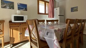 A dining area with wooden chairs and a table covered with a floral tablecloth. There is a microwave on a wooden cabinet, and a refrigerator is visible in the background. - 100m from ski slopes, 2nd floor, balcony, ski locker, 48m², Valfréjus (Valfréjus)