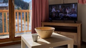 A room with a wooden table, a television, and a view of a mountain landscape through a sliding glass door. - 100m from ski slopes, 2nd floor, balcony, ski locker, 48m², Valfréjus (Valfréjus)