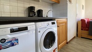 A compact kitchen with wooden cabinets, a washing machine, a microwave, and a coffee maker. - 100m from ski slopes, 2nd floor, balcony, ski locker, 48m², Valfréjus (Valfréjus)