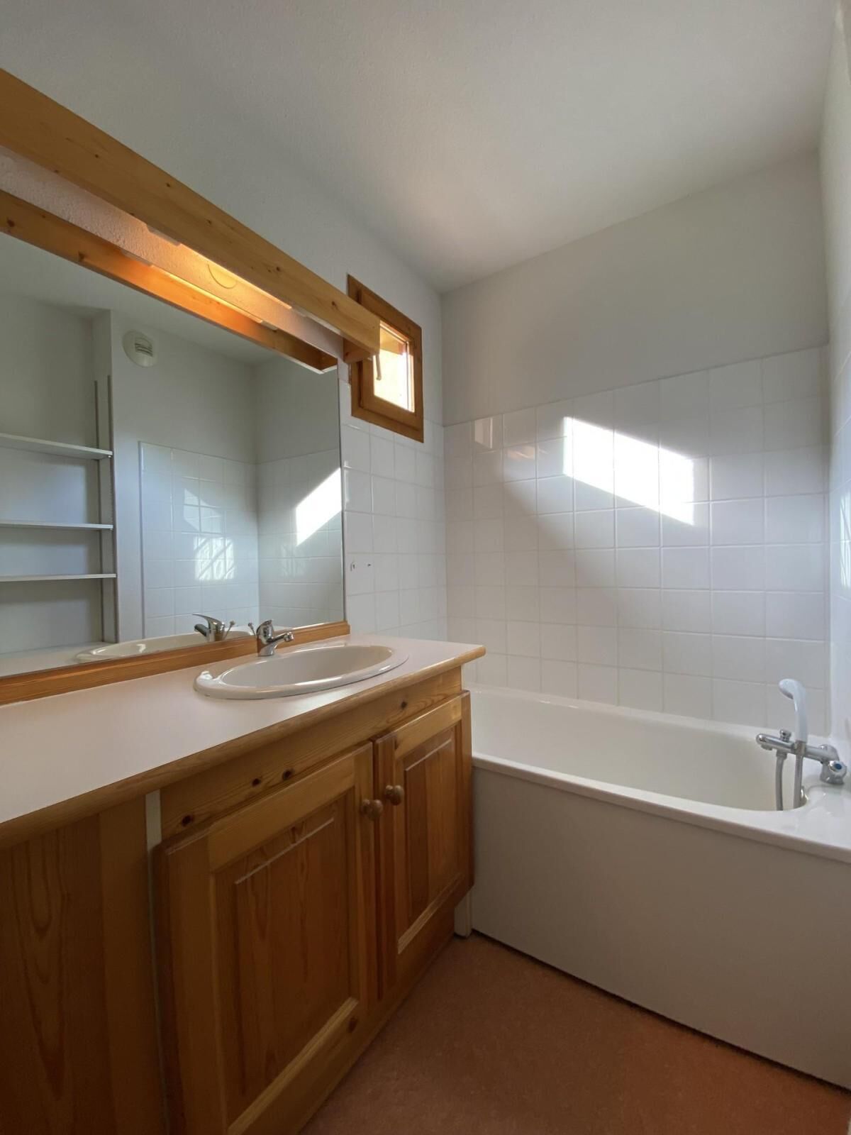 A bathroom with a wooden vanity, a large mirror, a white sink, and a bathtub.