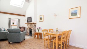 A cozy living room with a fireplace, a dining area with wooden chairs, and a sofa. - Bwthyn Taid (Holywell)
