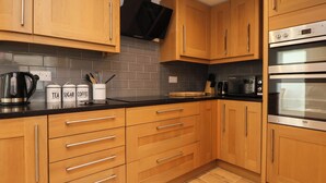 A modern kitchen with wooden cabinets, a black countertop, and stainless steel appliances including an oven and a microwave. - Bwthyn Taid (Holywell)