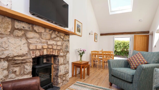 A cozy living room with a stone fireplace, a flat-screen TV, a sofa, and a dining table. - Bwthyn Taid (Holywell)
