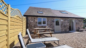 A stone building with a wooden fence, a picnic table, and two lounge chairs. - Bwthyn Taid (Holywell)