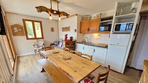 A kitchen with a wooden table, chairs, a hanging light fixture, and white cabinets.