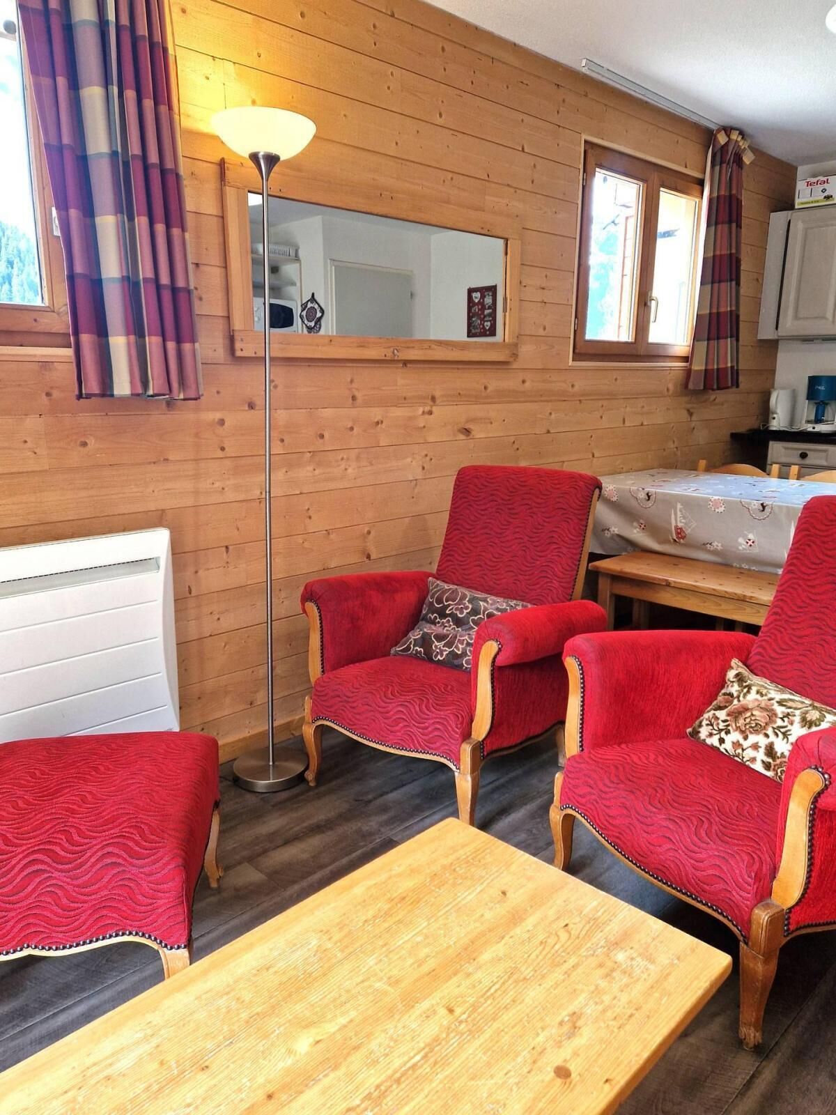 A cozy room with wooden walls, a red upholstered armchair, a matching ottoman, and a wooden table.
