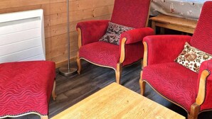 A cozy room with wooden walls, a red upholstered armchair, a matching ottoman, and a wooden table. - 100m from ski slopes, terrace, ski locker, 48m², Valfréjus (Valfréjus)