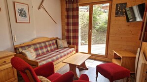 A cozy room with a wooden sofa, red armchairs, a wooden table, and a sliding glass door to an outdoor area. - 100m from ski slopes, terrace, ski locker, 48m², Valfréjus (Valfréjus)