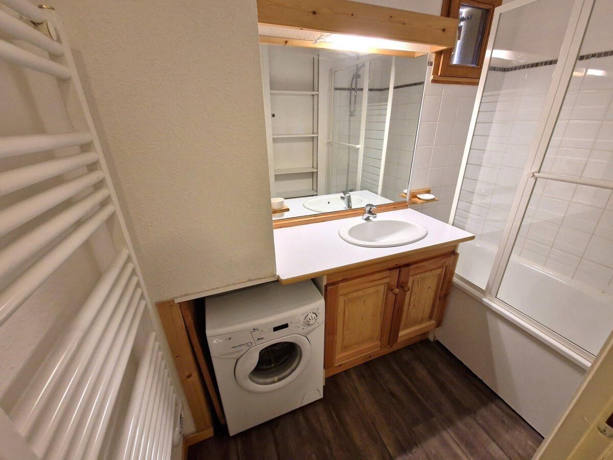 Een kleine badkamer met een wasmachine, wastafel en douche.