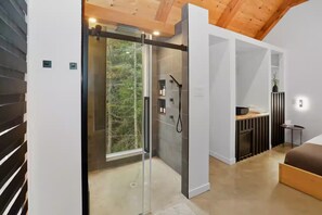 A modern interior with a glass door leading to a shower area, a kitchen with a dining table, and a sofa.
