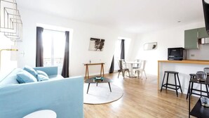 A modern living room with a blue sofa, a dining area with a small table and chairs, and a kitchen area with a counter and stools. - PARISIAN ESCAPE NEXT TO THE LOUVRE AND PALAIS ROYAL - RUE SAINT-HONORÉ (Paris)