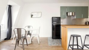 A modern kitchen with a black refrigerator, a wooden island, and green cabinets. - PARISIAN ESCAPE NEXT TO THE LOUVRE AND PALAIS ROYAL - RUE SAINT-HONORÉ (Paris)