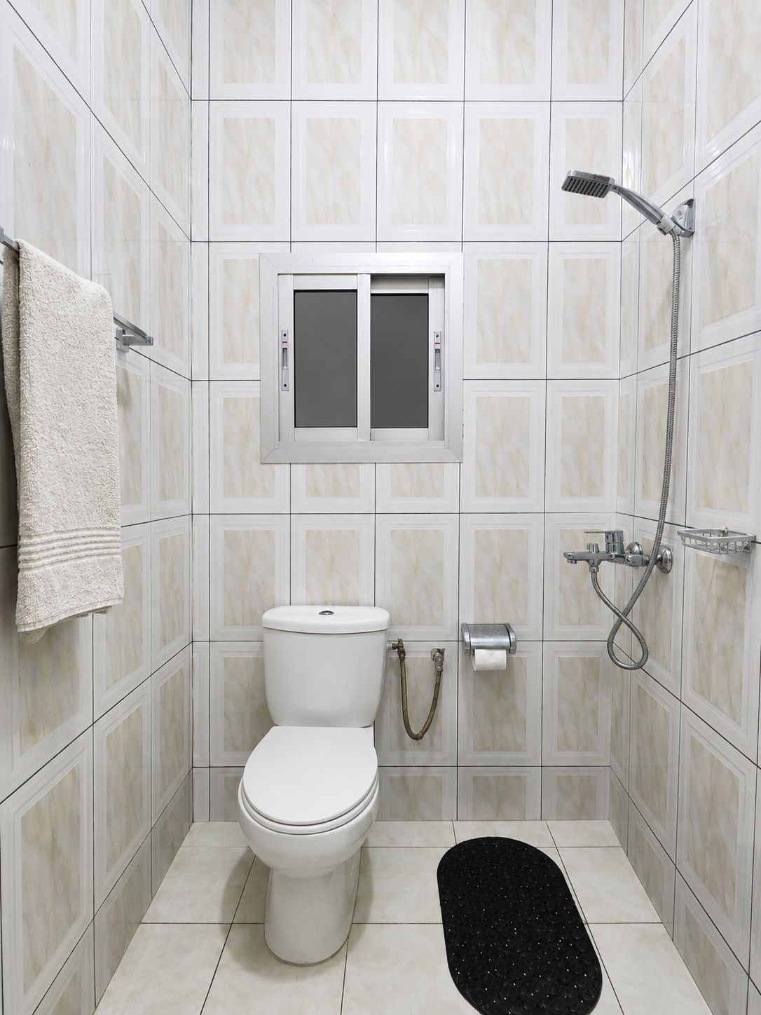 Un baño pequeño con azulejos, un inodoro, una ducha y un tendedero para toallas.