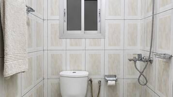 Un baño pequeño con azulejos, un inodoro, una ducha y un tendedero para toallas.
