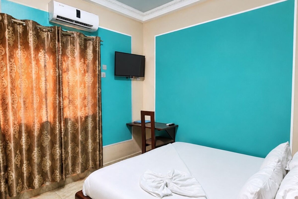 A hotel room with a bed, a television, a desk, and an air conditioning unit.