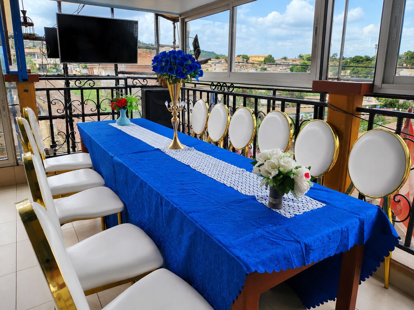 Un comedor con mantel azul, sillas blancas, un candelabro dorado y un ramo de flores.