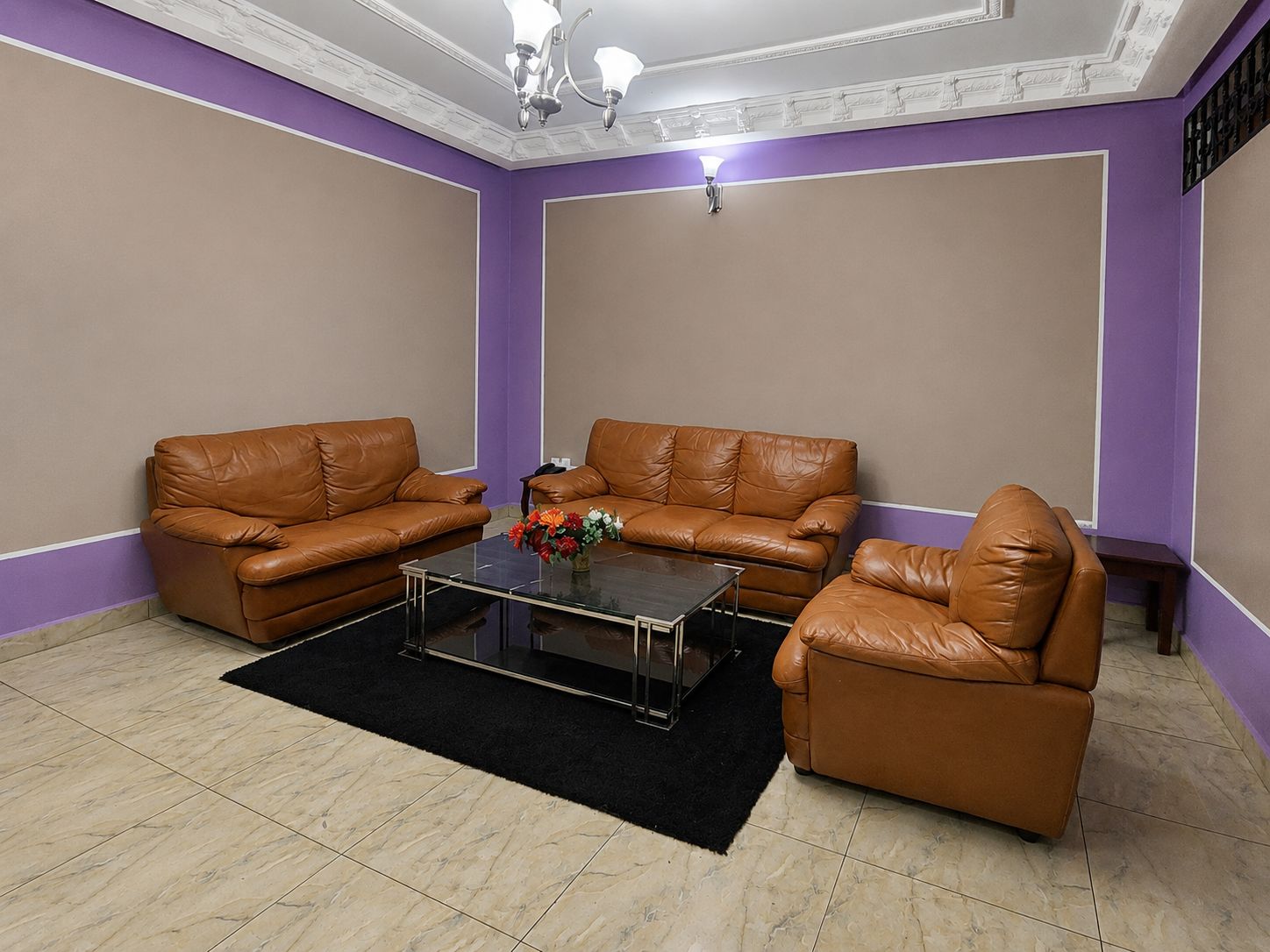 A room with two brown leather sofas, a glass coffee table, and a black rug.