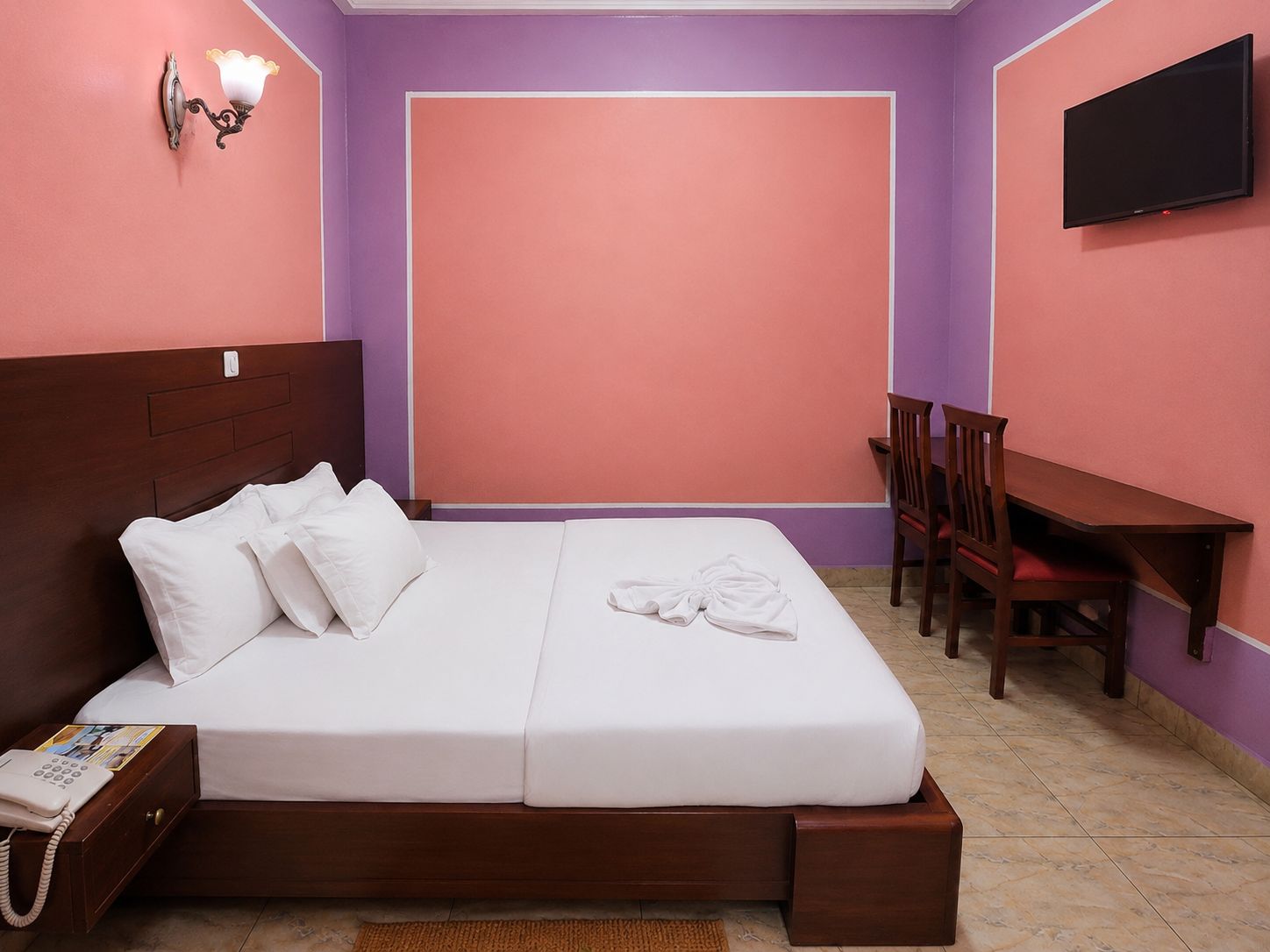 Un dormitorio con cama, teléfono junto a la cama y escritorio con silla.