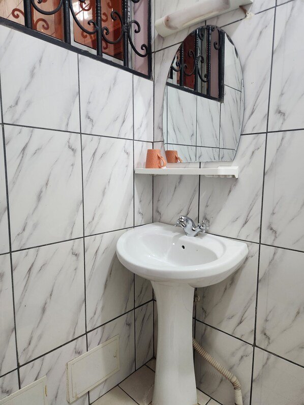 A bathroom with a white marble sink, a mirror, and a towel rack. - Hotel Residence Madadjeu (Yaoundé)
