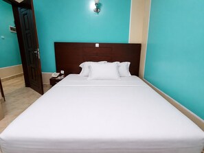 Una habitación de hotel con una cama grande, una mesita de noche con teléfono y una lámpara de pared.