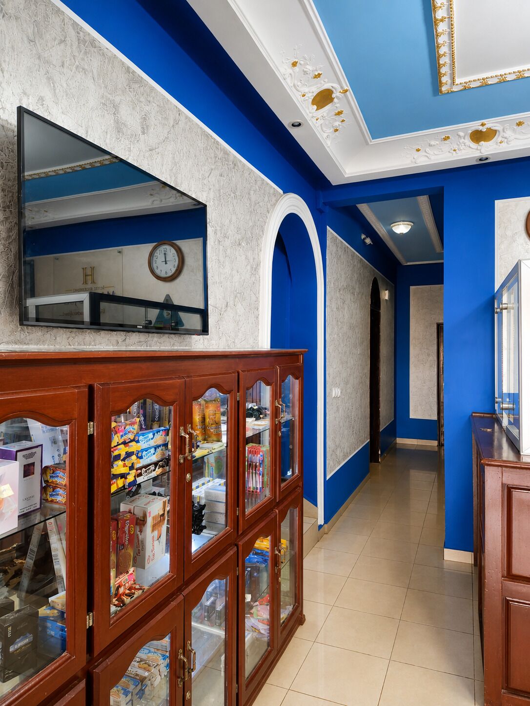 A hallway with a clock, a wooden cabinet with glass doors, and blue walls.