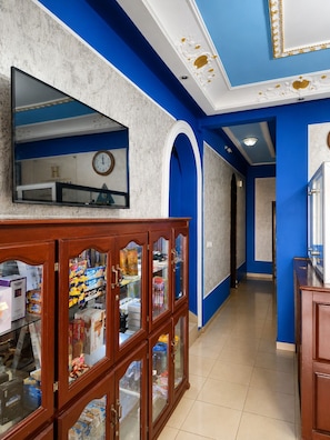 A hallway with a clock, a wooden cabinet with glass doors, and blue walls. - Hotel Residence Madadjeu (Yaoundé)