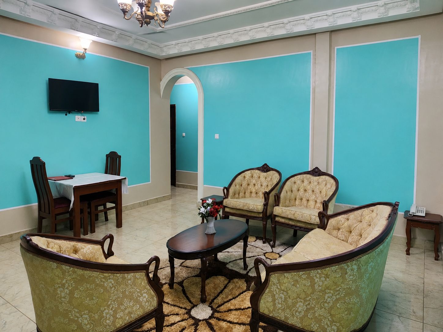 A room with a dining table, two chairs, a sofa, and a television.