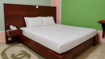 Una cama individual con cabecera de madera, un teléfono en la mesita de noche y una pared verde.