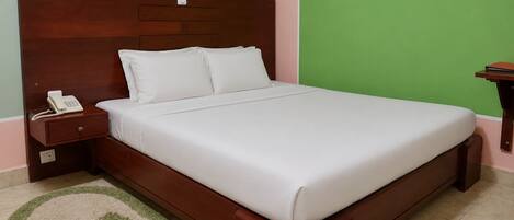 A single bed with a wooden headboard, a bedside telephone, and a green wall.