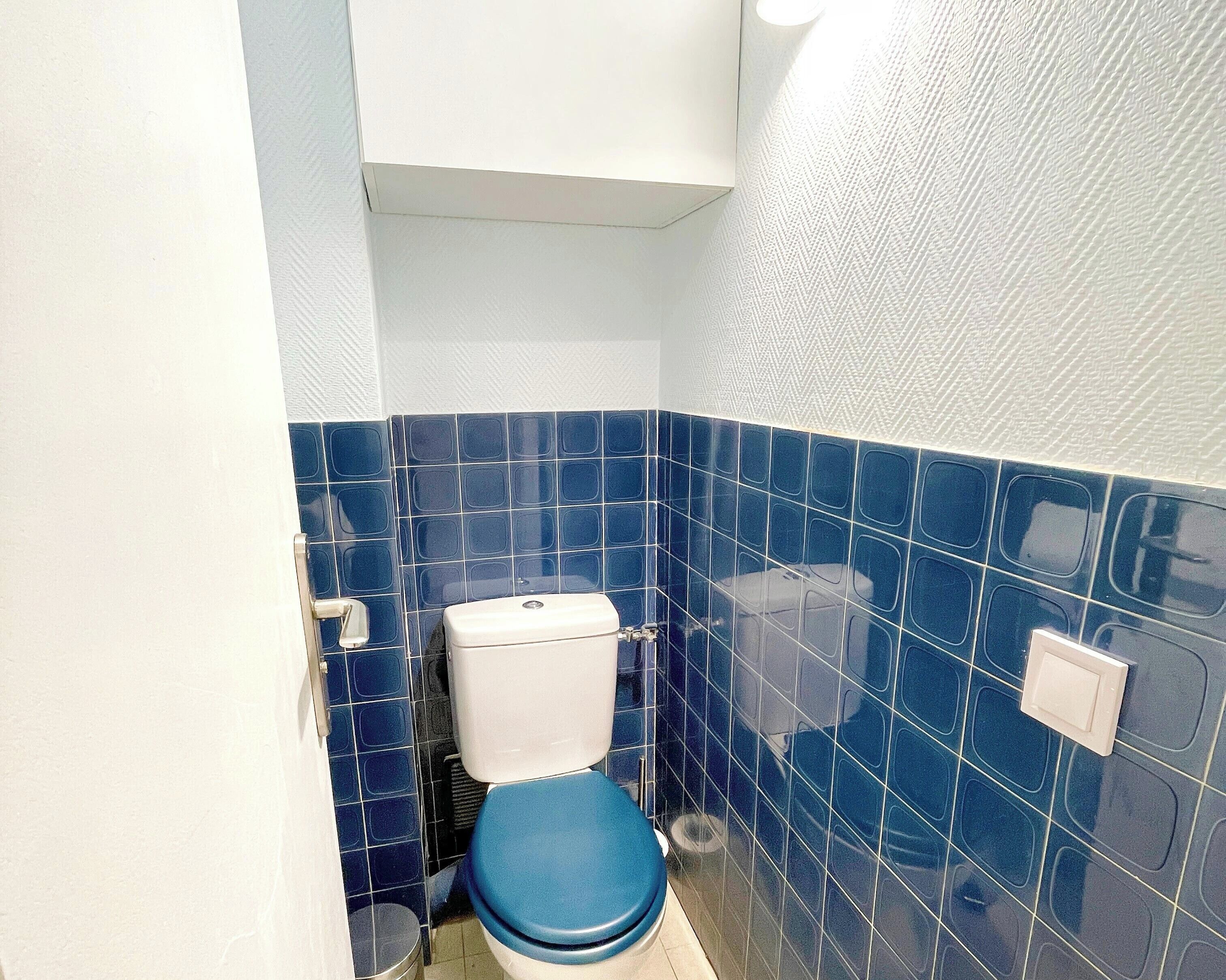 A small bathroom with a toilet, a trash bin, and a wall with blue tiles.