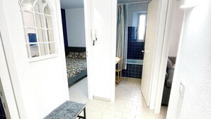 A narrow hallway with a bed, a small table, and a bathroom visible through an open door. - Apartment with balcony - sea view (Canet-en-Roussillon)