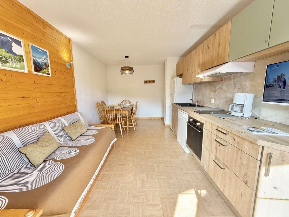 A modern kitchen with wooden cabinets, a dining area with a wooden table and chairs, and a sofa with patterned cushions.