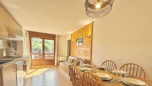 A modern kitchen with wooden cabinets, a dining area with a wooden table set for four, and a large sliding glass door leading to an outdoor area. - 140m from ski slopes, 2nd floor, view mountain, balcony, ski locker, 37m², Flumet (Flumet)