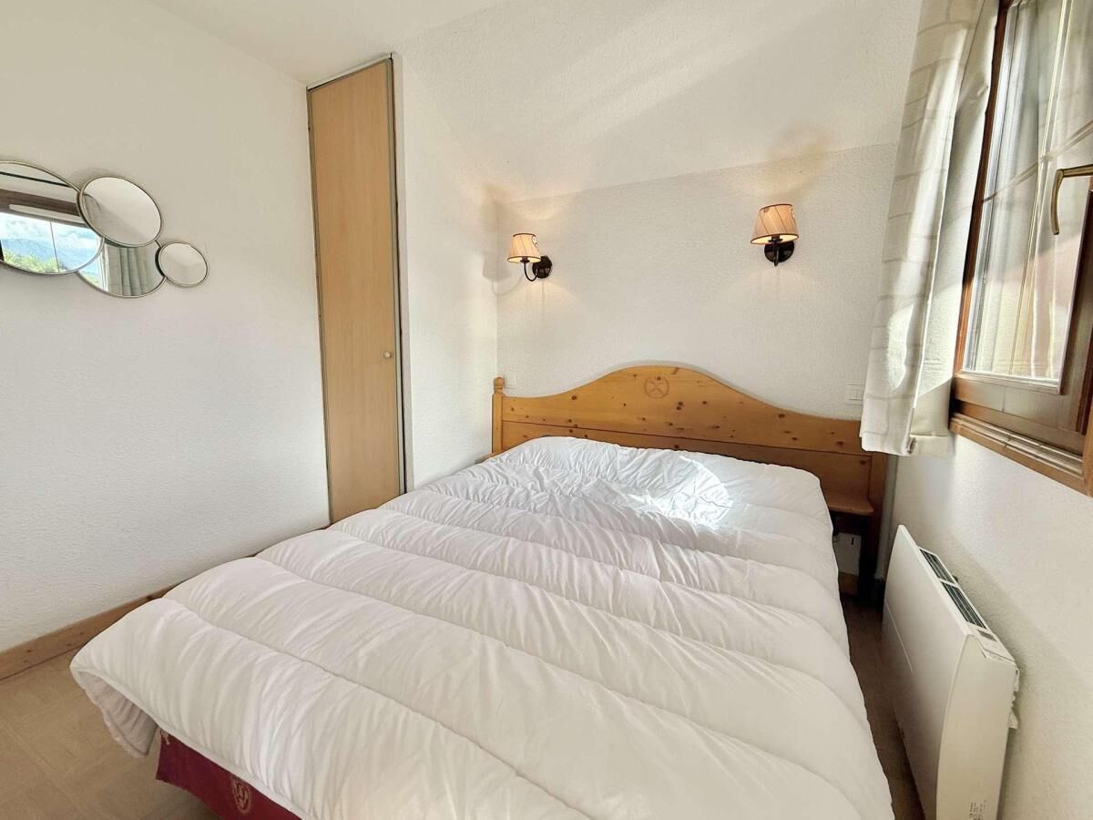 A bedroom with a wooden headboard, a white bedspread, two wall-mounted lamps, and a window with curtains.