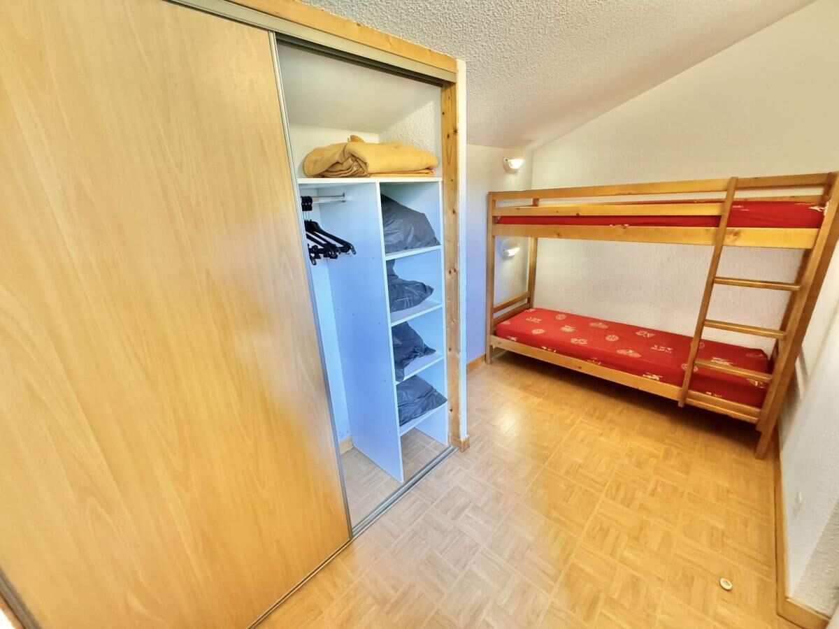 A room with a bunk bed, a wardrobe with open doors, and a wooden floor.