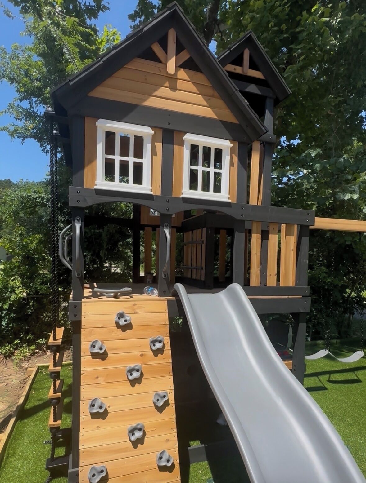 Une cabane en bois pour enfants, avec un toboggan, un mur d’escalade et des fenêtres.