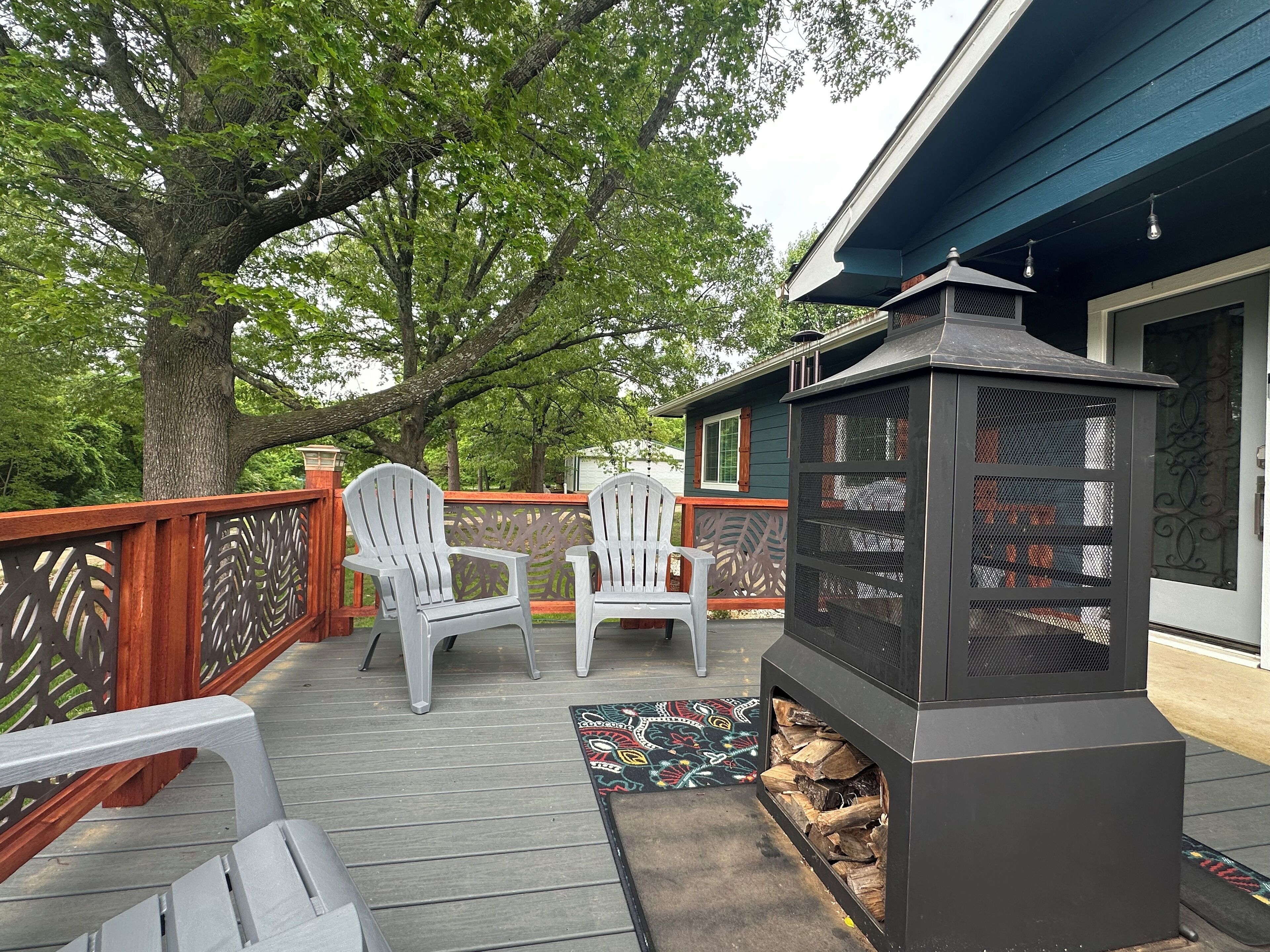 A deck with two white Adirondack chairs, a decorative rug, and a wood-burning stove.