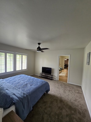 A bedroom with a bed, a ceiling fan, a TV on a stand, and a doorway leading to another room. - Sunset Drive! (Wewoka)