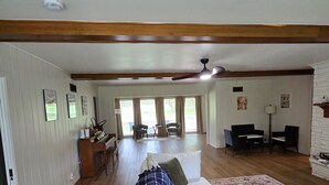 A spacious living room with a large sofa, a piano, and a dining area with chairs. - Sunset Drive! (Wewoka)