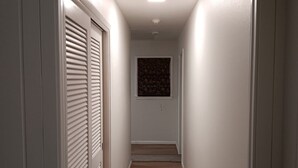 A narrow hallway with a wooden floor, white walls, and a ceiling light. - Sunset Drive! (Wewoka)