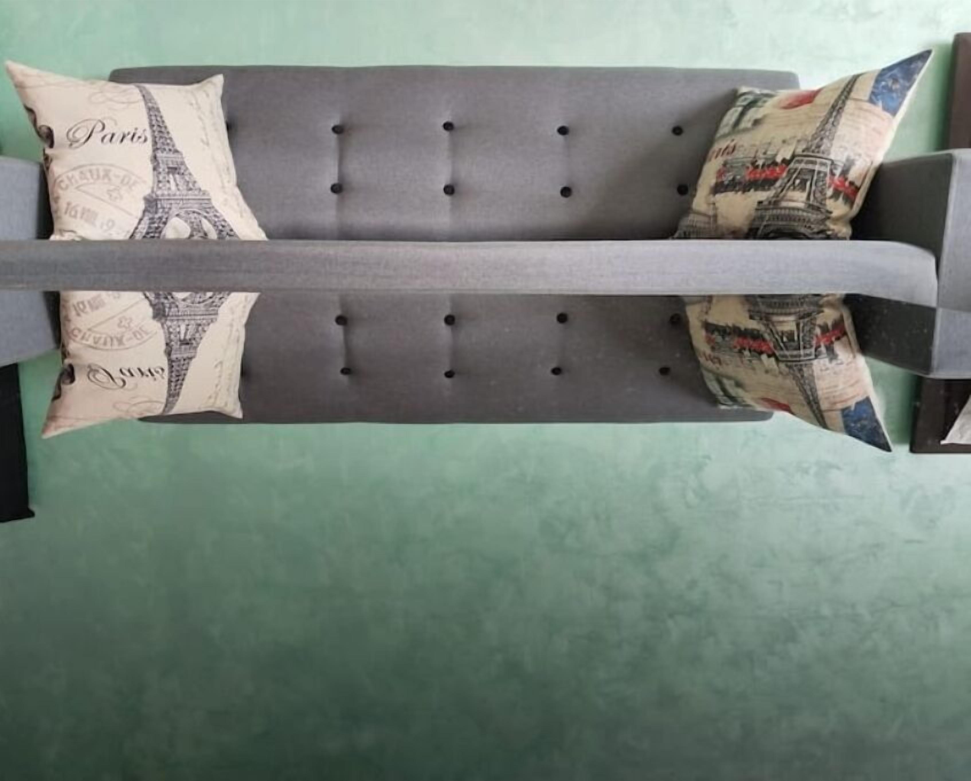 Un canapé gris recouvert d’un tissu d’ameublement, orné de quatre boutons noirs et agrémenté de deux coussins décoratifs représentant la Tour Eiffel.