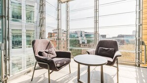 Ein modernes Zimmer mit zwei Sesseln, einem kleinen Tisch, großen raumhohen Fenstern und Blick auf die Stadt.