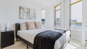 Ein modernes Schlafzimmer mit einem großen Bett, einem Nachttisch und einem Fenster mit Blick auf die Stadt.