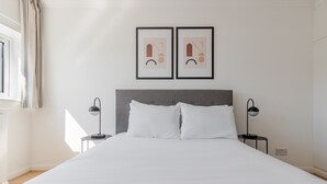 A neatly made bed with white linens, a grey upholstered headboard, and two bedside tables with black lamps. - Blueground | Bayswater, balcony & w/d, nr parks (London)