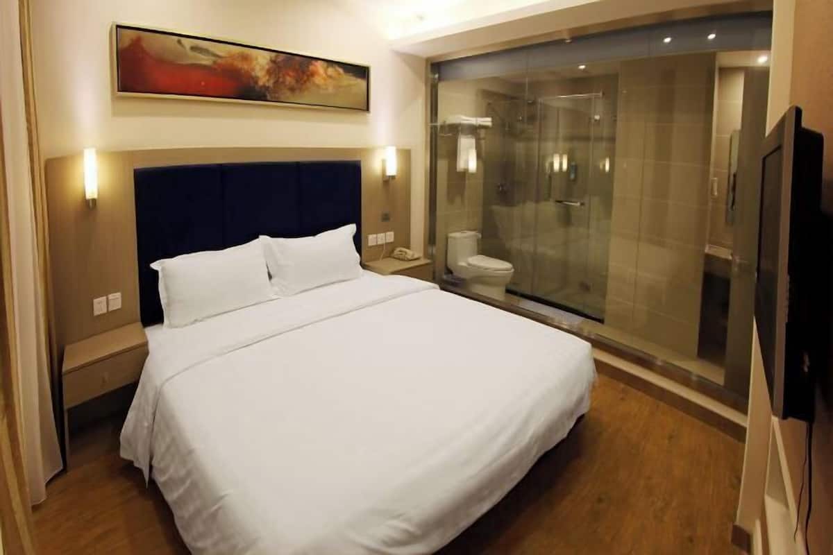 A hotel room with a large bed, a glass-enclosed shower, and a painting on the wall.