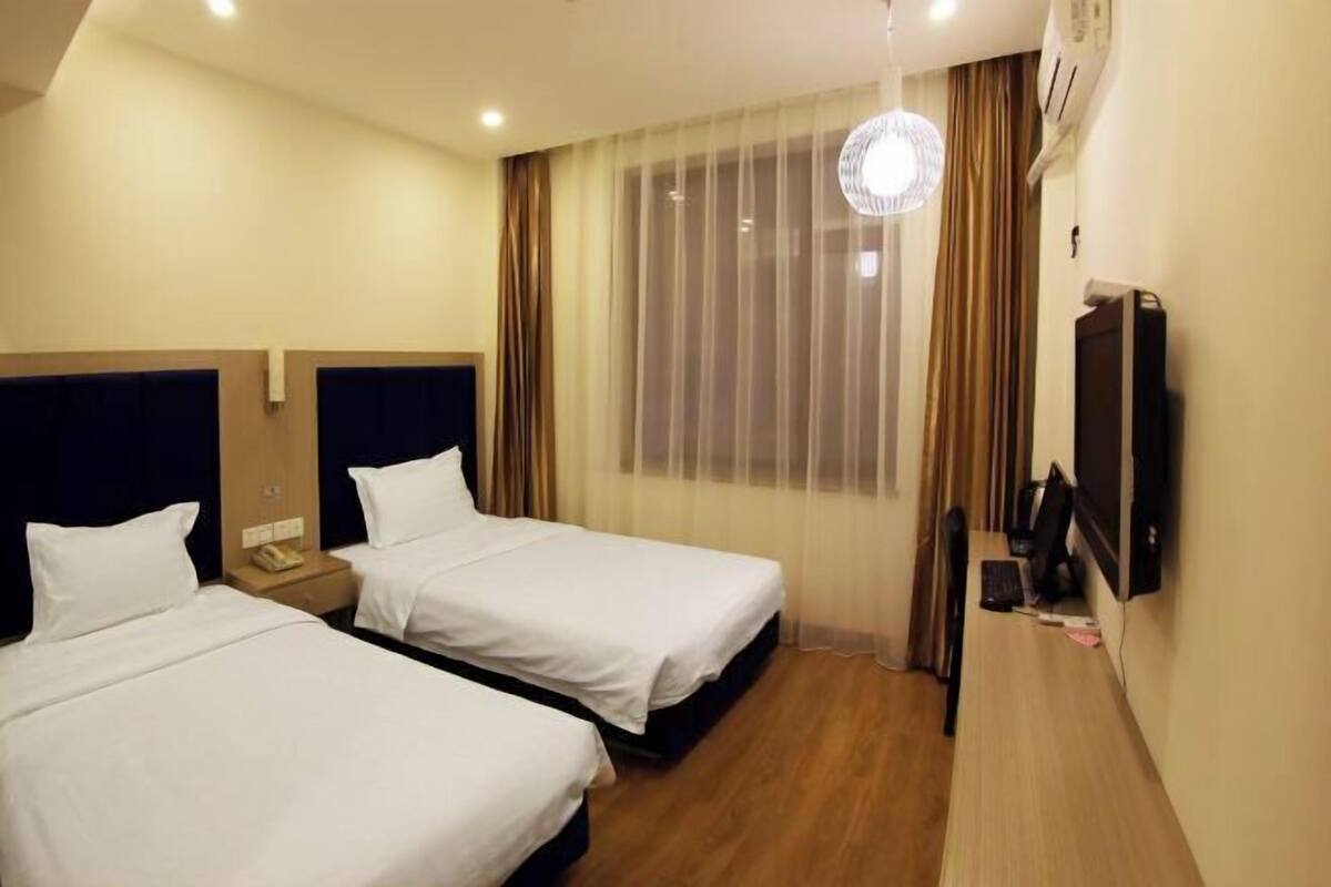 A hotel room with two beds, a desk with a computer, a TV, and a window with curtains.