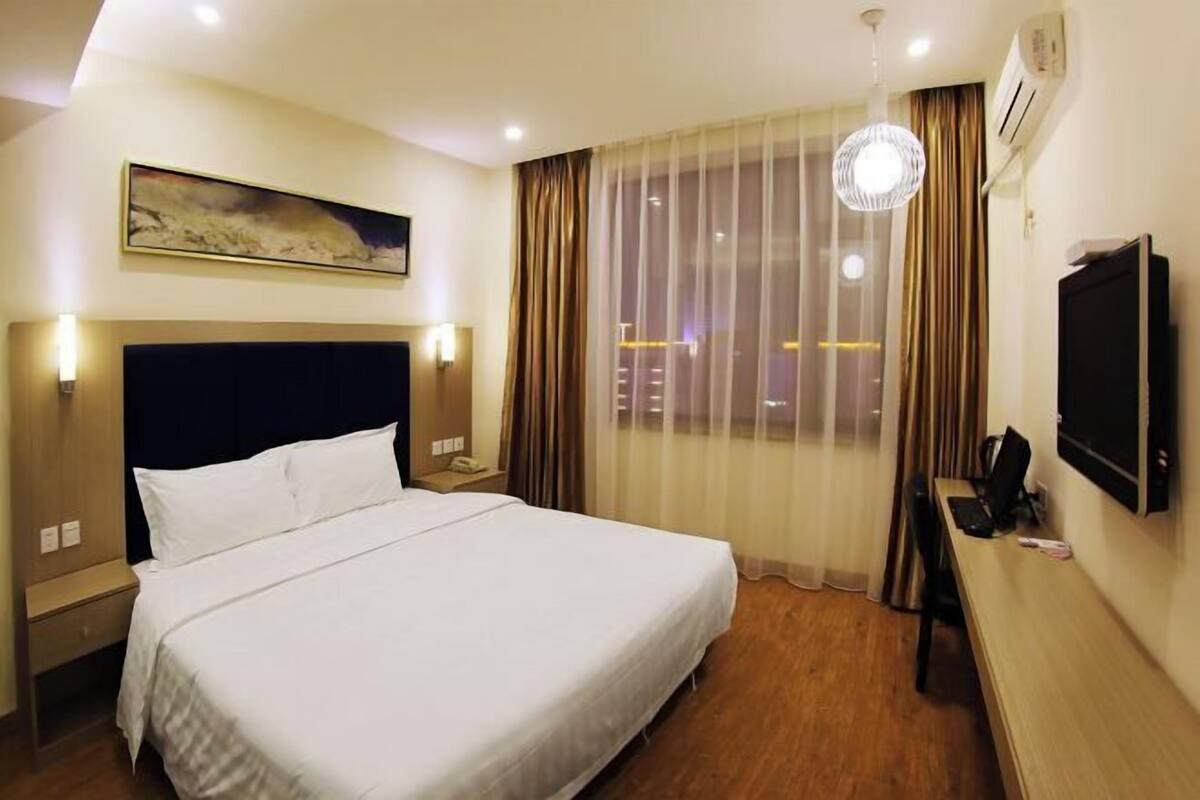 A hotel room with a bed, a desk, a TV, and a window with curtains.