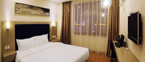 A hotel room with a bed, a desk, a TV, and a window with curtains.